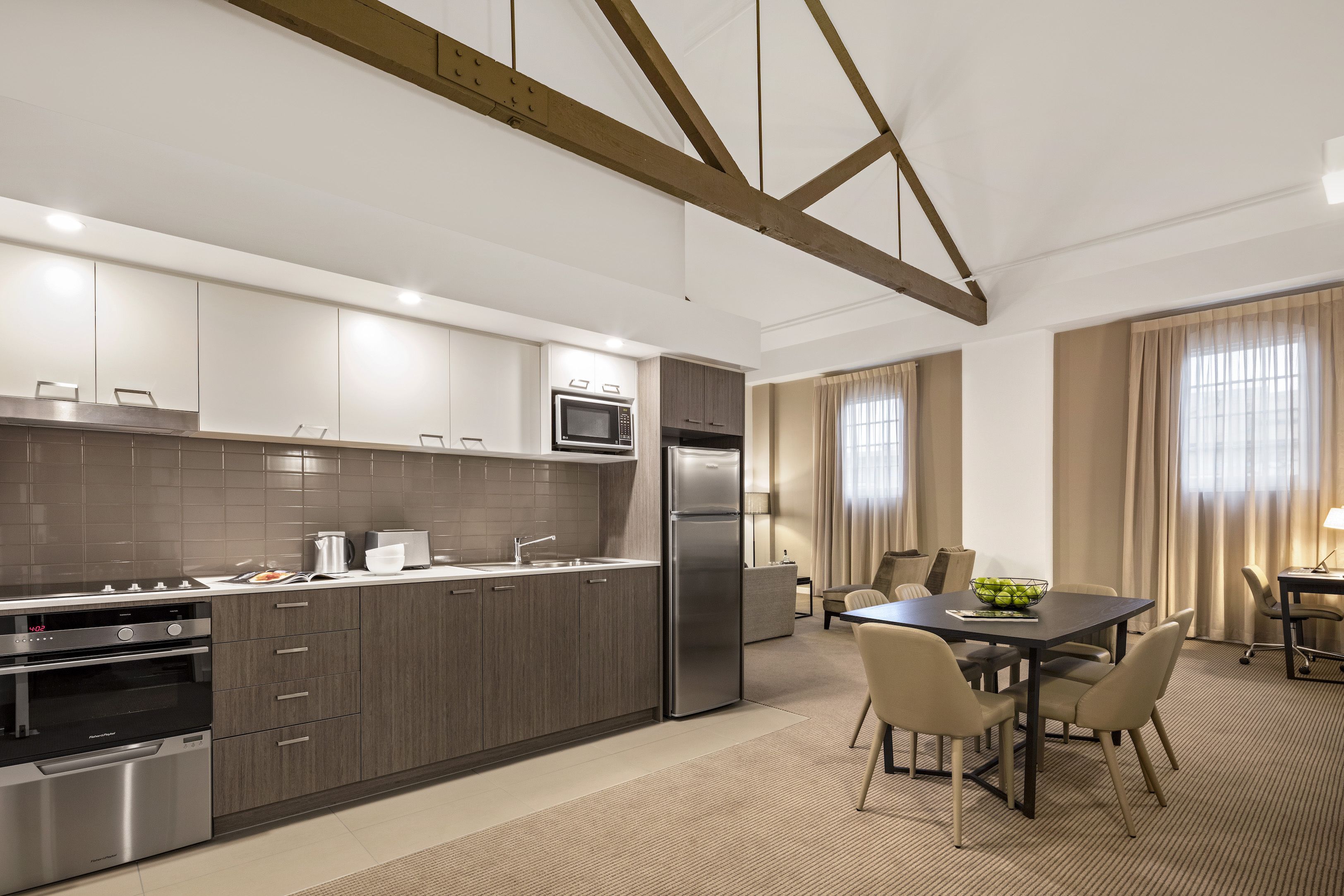 A modern kitchen with stainless steel appliances, a dining area with a table and chairs, and a view of the living area with curtains.