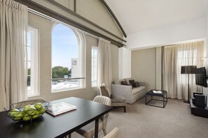A modern hotel room with a large window, a sofa, a dining table with a bowl of apples, and a TV. - Quest Newcastle West (Newcastle West)