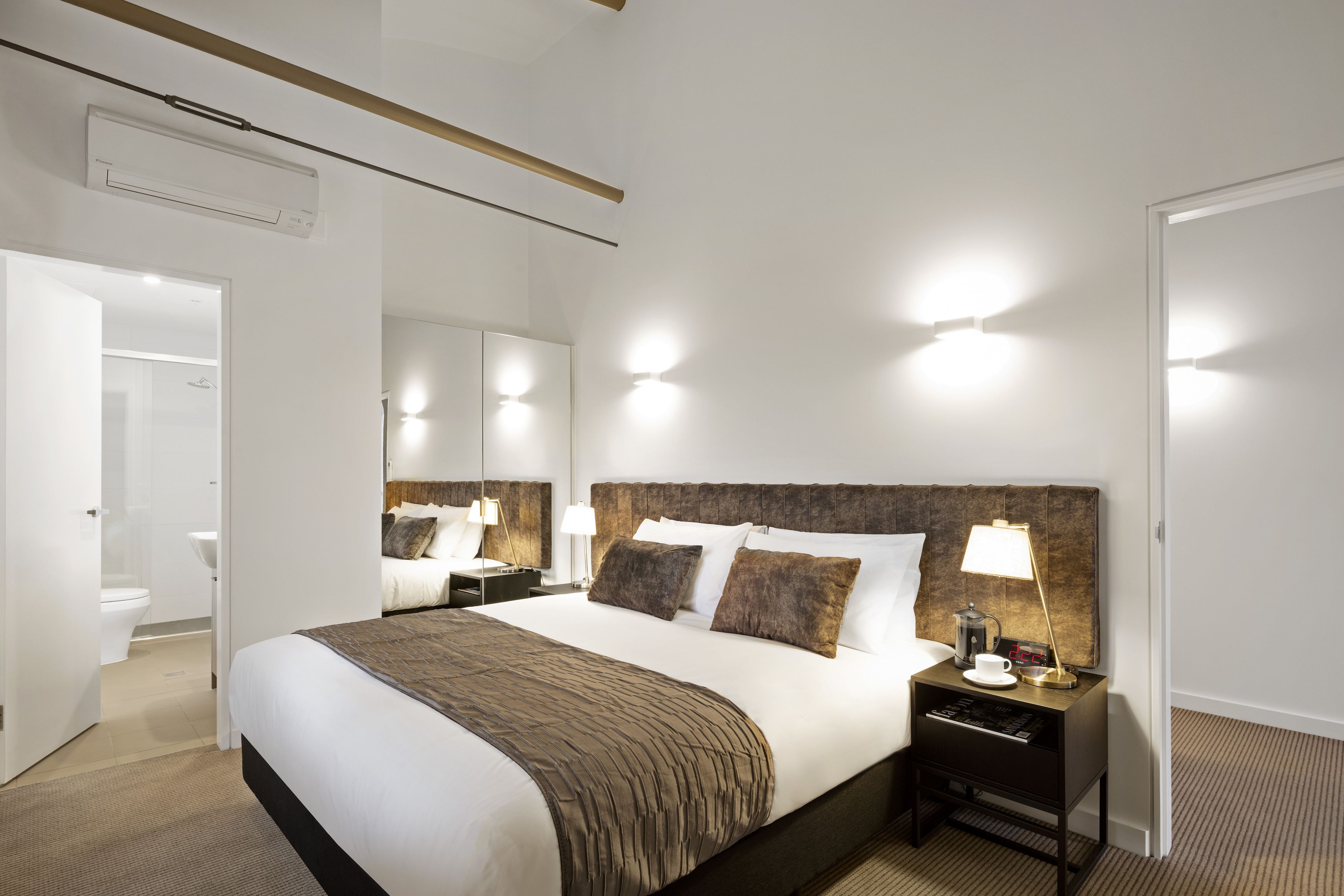 Ein Hotelzimmer mit einem großen Bett, Nachttischlampen, einem Nachttisch und einem durchgehenden Türspalte sichtbaren Badezimmer.
