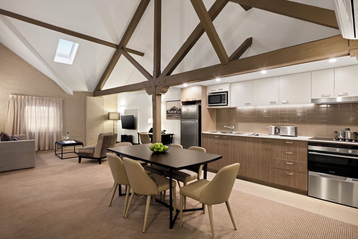 A modern kitchen with built-in appliances, a dining area with a table and chairs, and a living room with a sofa and a TV.