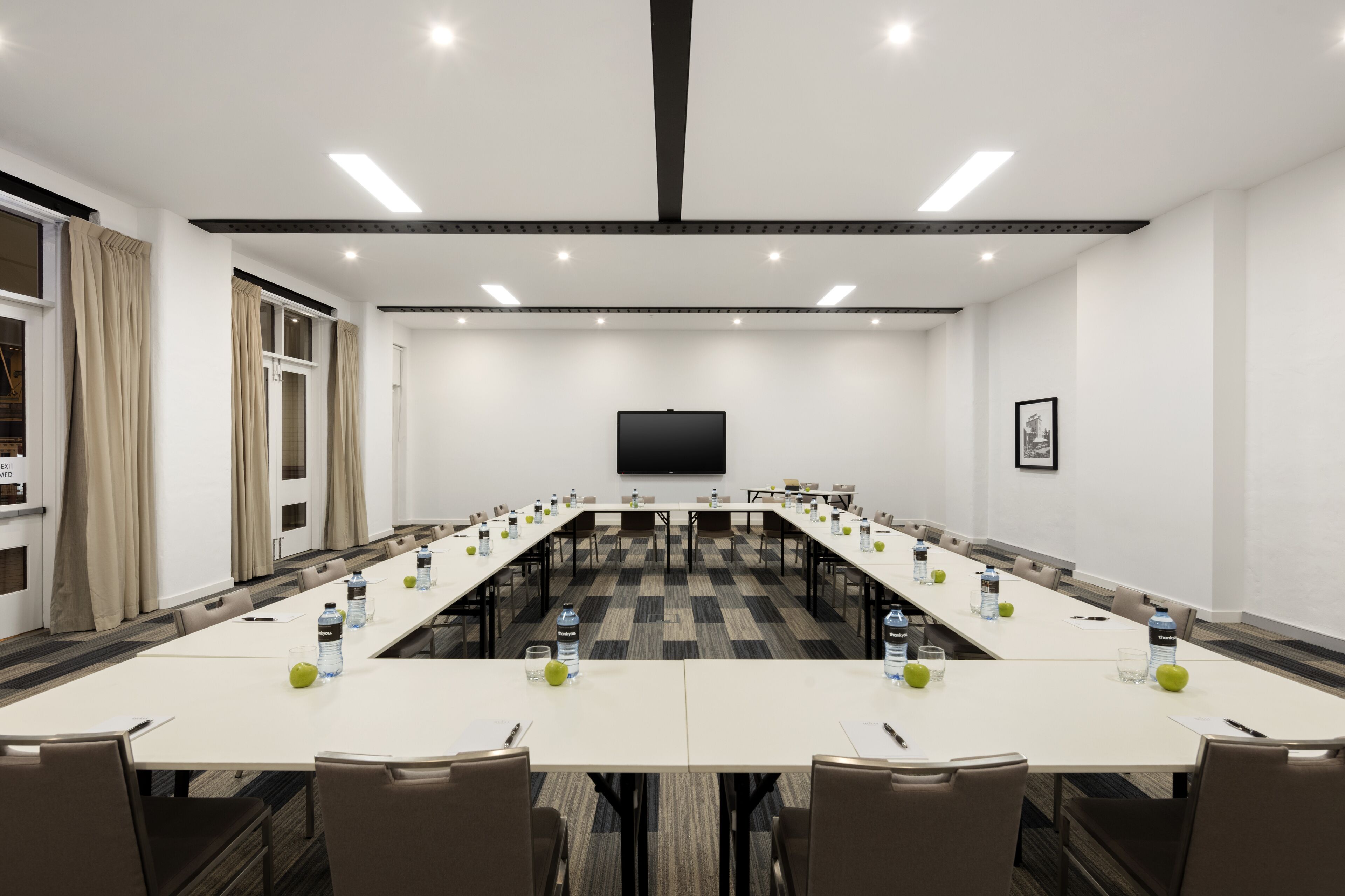 A conference room with a long table, chairs, a flat-screen TV, and a door with curtains.