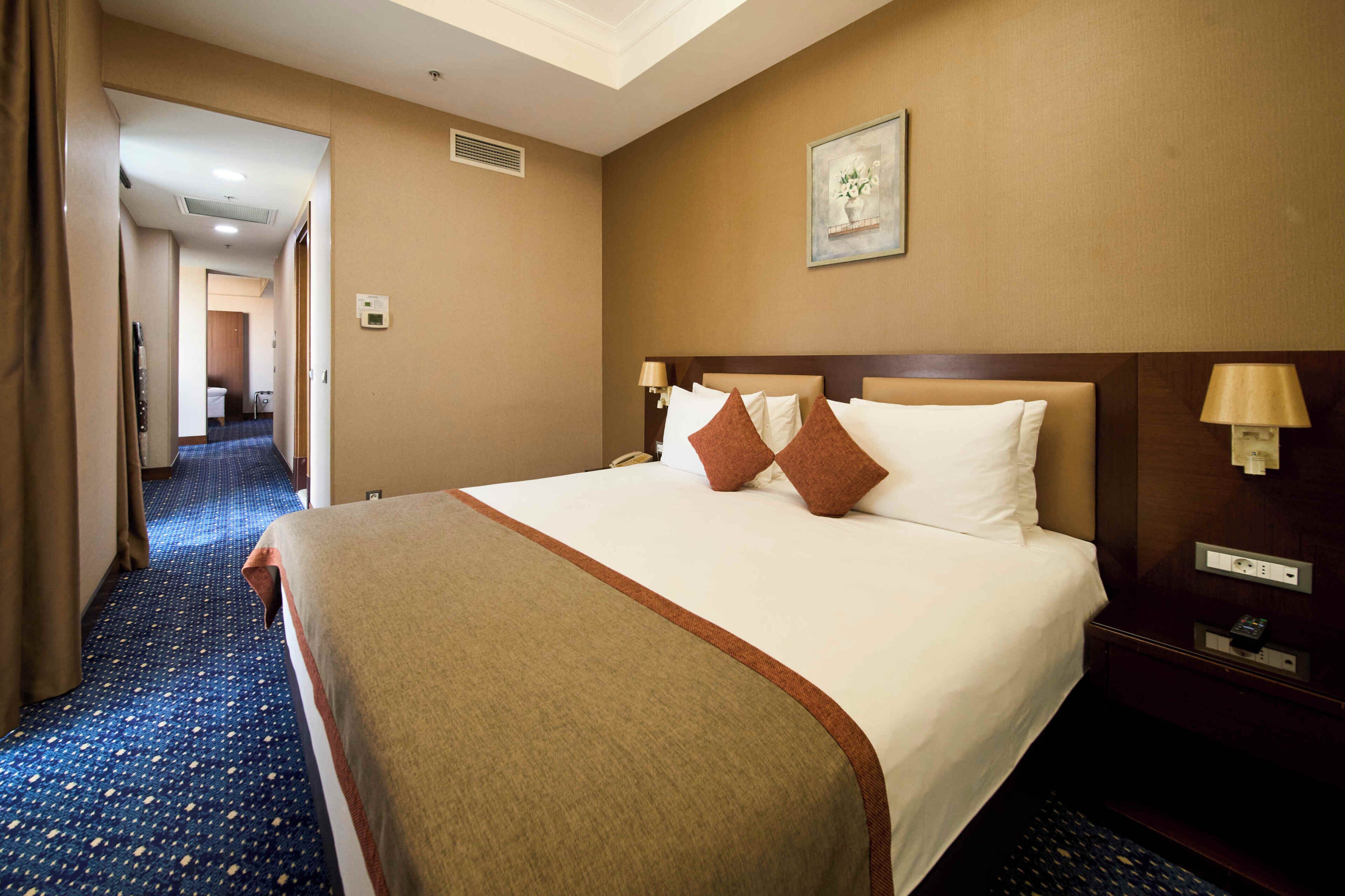 Habitación de hotel con una cama grande, cabecera, lámparas de noche, mesitas de noche y suelo alfombrado.