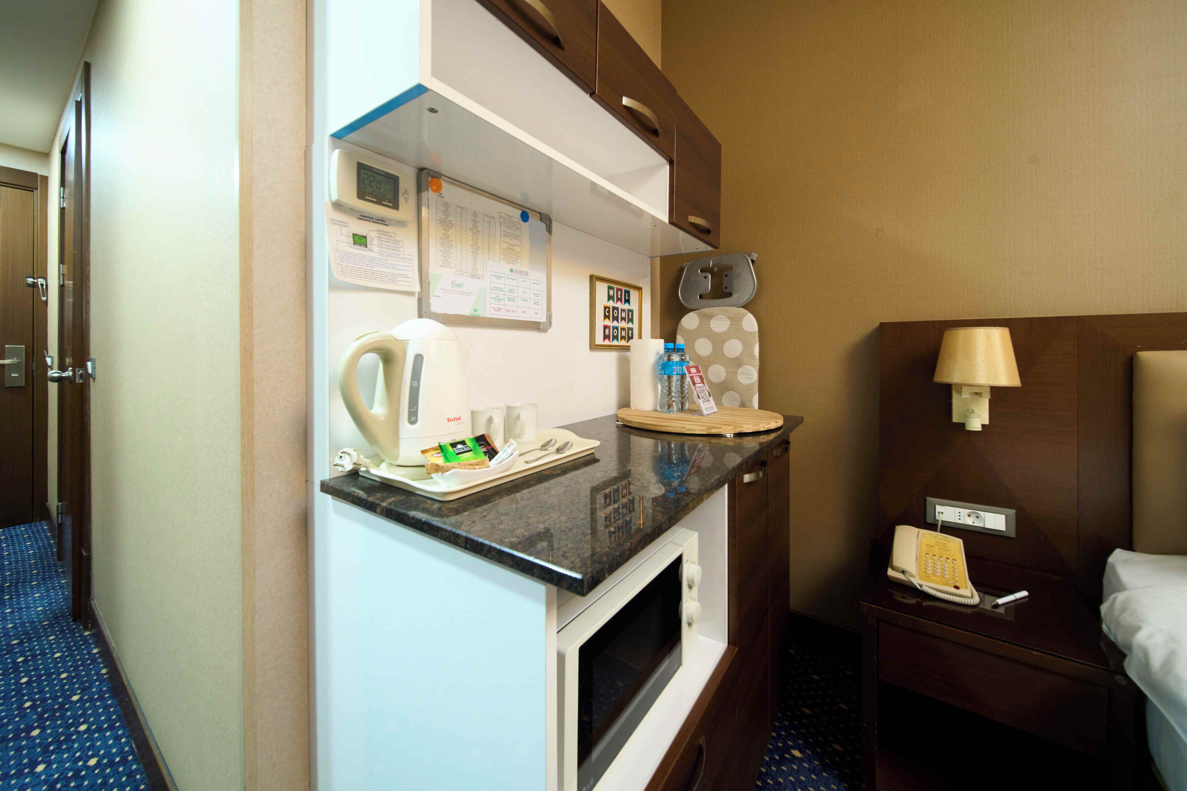 Habitación de hotel con kitchenette, microondas, cafetera, teléfono y mesita de noche con lámpara.