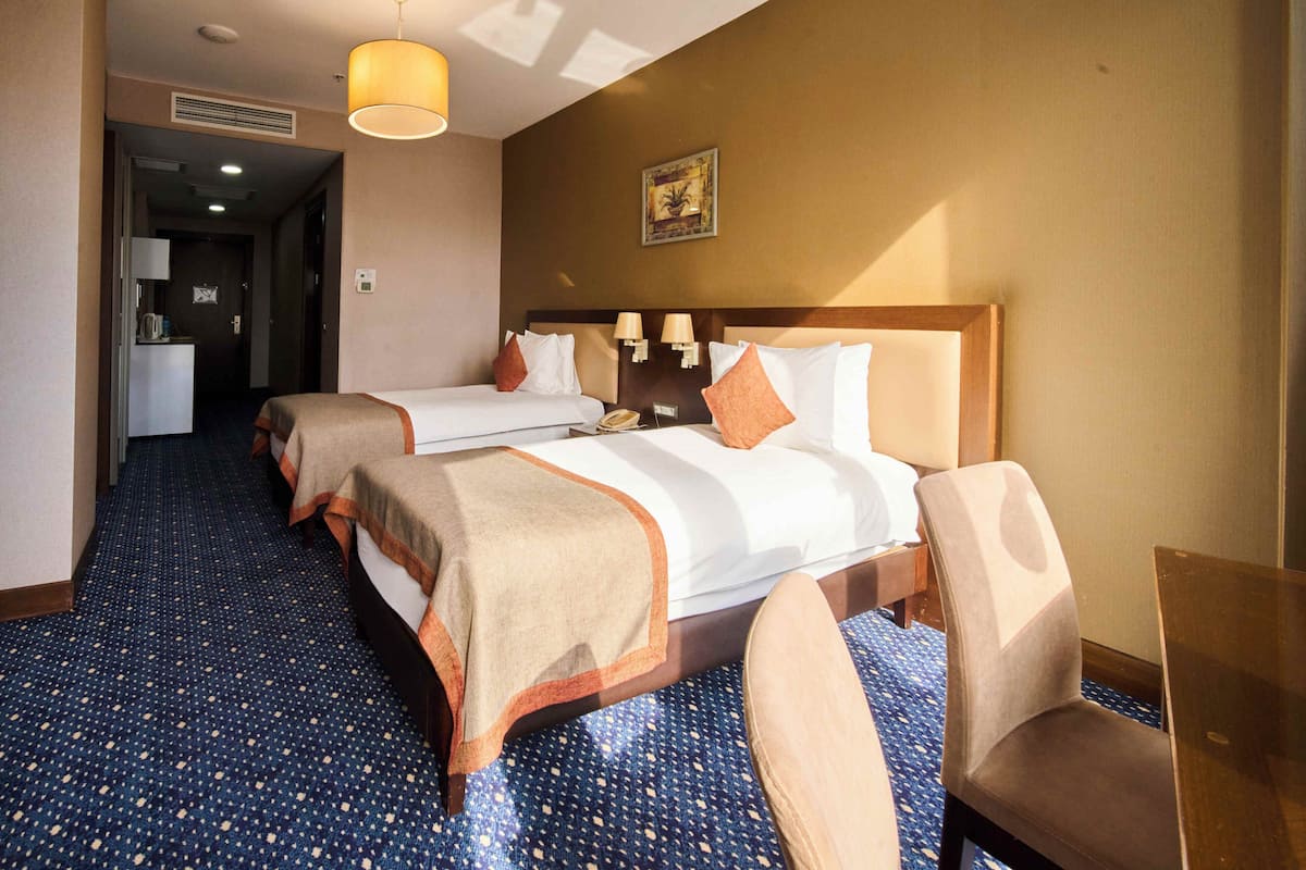 A hotel room with two beds, a desk, a chair, a lamp, and a picture on the wall.