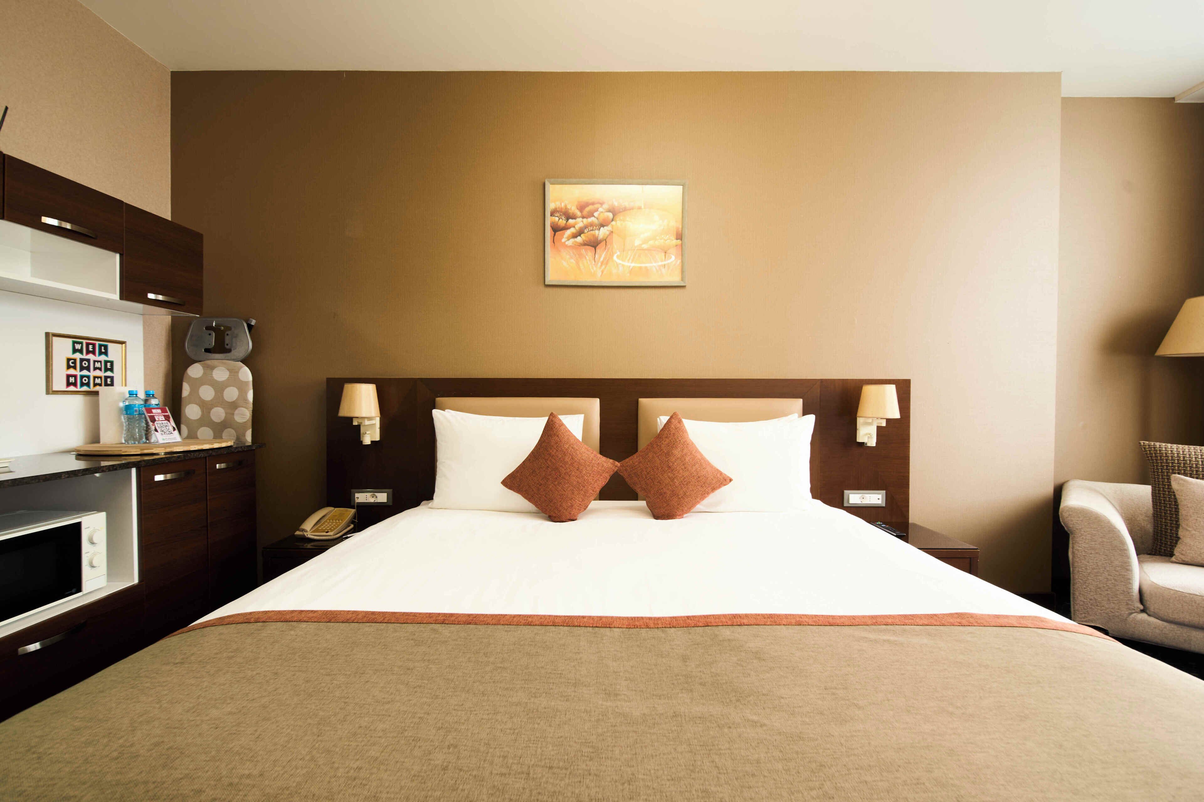 A hotel room with a large bed, a desk with a telephone, a microwave, and a small cabinet.