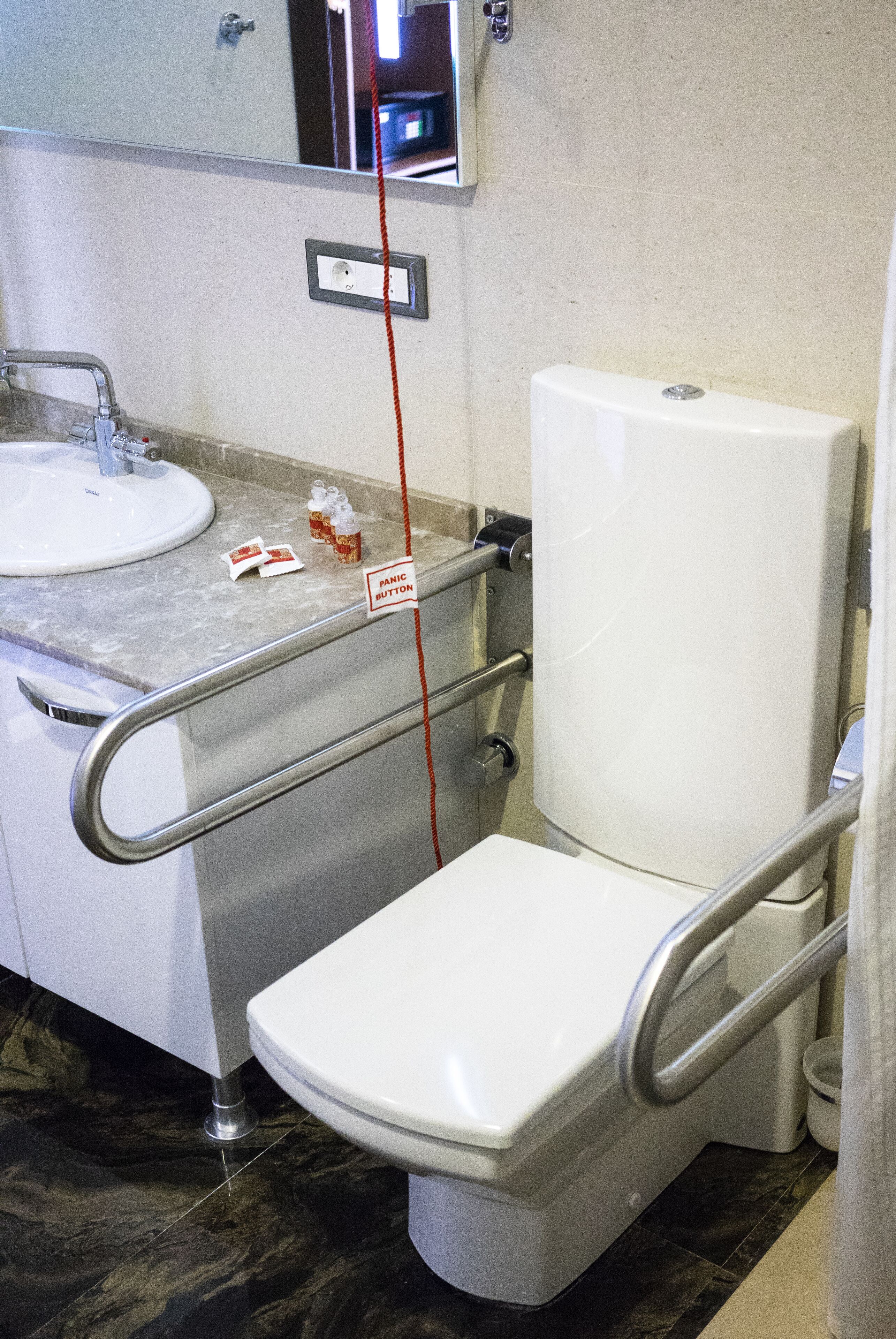 A bathroom with a white toilet, a sink, and a mirror. There is a red cord hanging from the mirror.