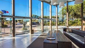 A modern interior with large windows, a wooden bench, and a sofa. - Sao Rafael Suites (Albufeira)