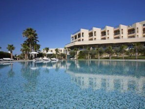 Ein Hotel mit großem Schwimmbad, Palmen und blauem Himmel.
