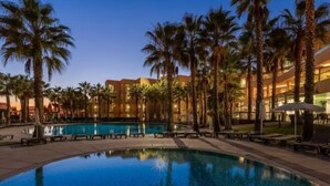 A poolside area with palm trees and a building in the background. - Sao Rafael Suites (Albufeira)