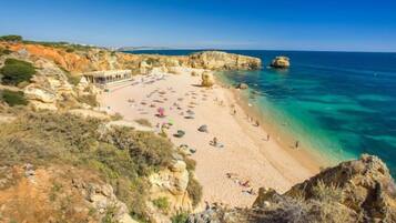 A coastal beach with clear waters, rocky cliffs, and a sandy shore.
