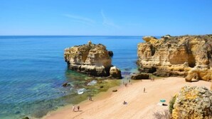 A beach with clear water, rocky formations, and people on the sand. - Sao Rafael Suites (Albufeira)