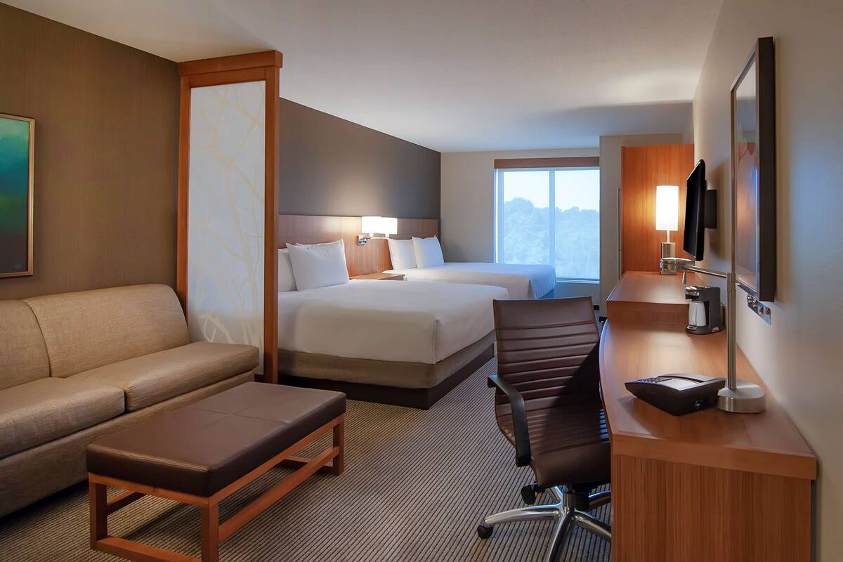 A hotel room with a bed, a sofa, a desk with a chair, and a TV.