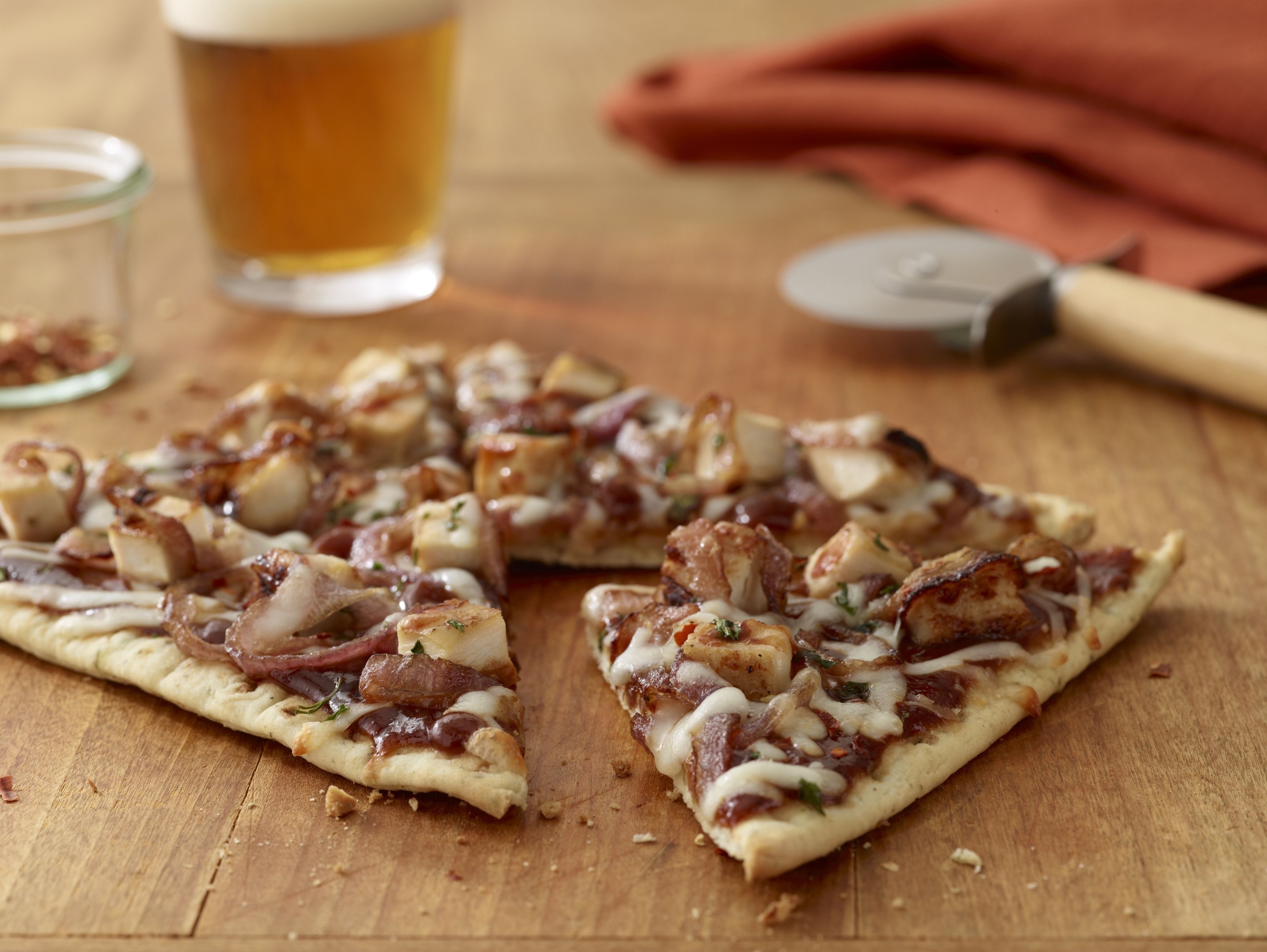 A pizza on a wooden surface with a beer glass and a knife in the background.
