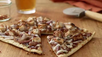 A pizza on a wooden surface with a beer glass and a knife in the background.