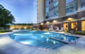 A swimming pool with a clear deck, surrounded by lounge chairs and a wooden fence.