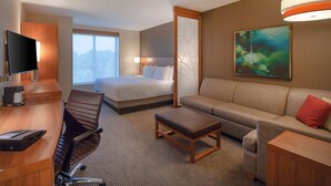 A hotel room with a bed, a sofa, a desk with a chair, a television, and a painting on the wall.