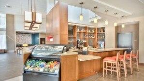 A modern bar area with a refrigerated display, wooden bar counter, and seating.