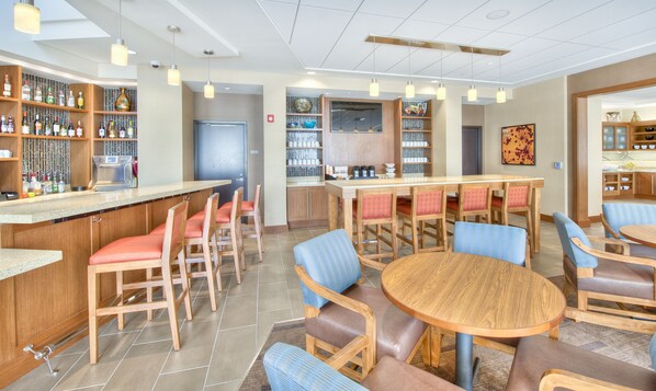 A modern bar area with wooden furniture, a counter with various bottles, and a seating area with round tables and chairs.