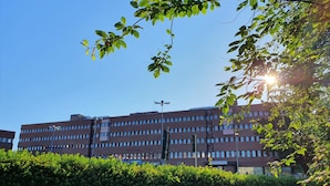 Un immeuble à plusieurs étages, doté d’un toit plat, entouré de verdure et surplombant un ciel dégagé.