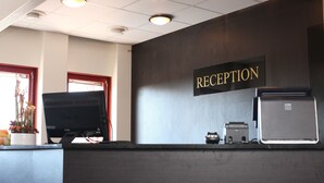 Un comptoir d’accueil équipé d’un écran, d’un petit réfrigérateur et d’une pancarte indiquant « RÉCEPTION ».