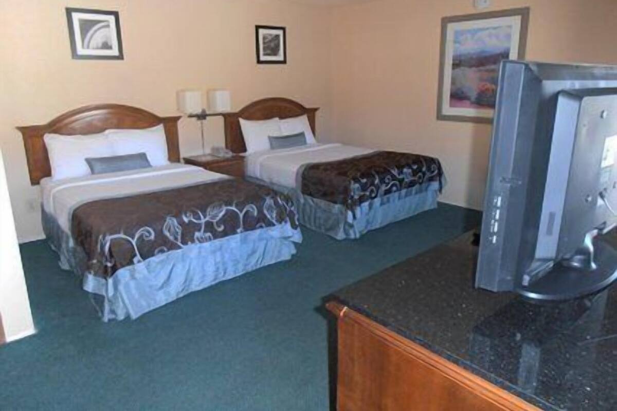 A hotel room with two beds, a desk, and a television.