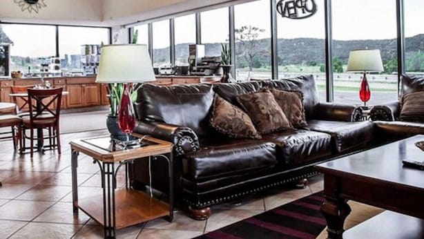 A spacious living room with a leather couch, a dining area with wooden furniture, and large windows offering a view of the outdoors. - Budget Host (Trinidad)