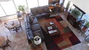 A spacious living area with a sofa, coffee table, and dining table. There are potted plants and a bookshelf in the background. - Budget Host (Trinidad)