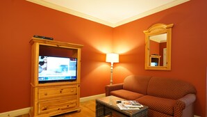 A living room with a wooden entertainment center, a sofa, a coffee table, and a lamp. - Southampton Long Island Hotel (Southampton)