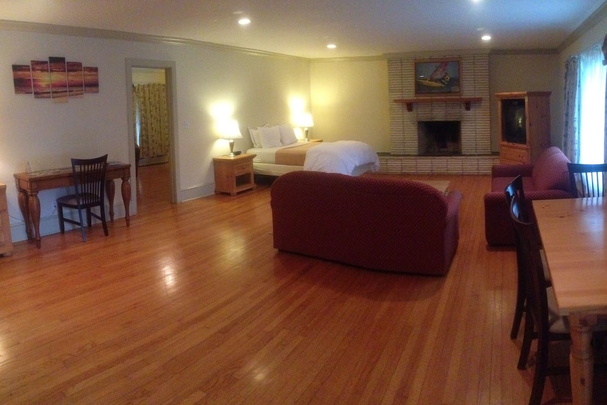 Ein Hotelzimmer mit Holzboden, einem roten Sofa, einem Bett, einem Kamin und einem Essbereich mit Tisch und Stühlen.