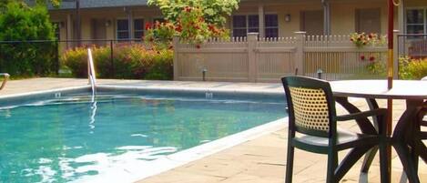 A swimming pool with a chair and table, surrounded by a fence and a building with windows.