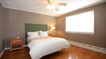 A bedroom with a bed, a nightstand, a lamp, a ceiling fan, and a window.