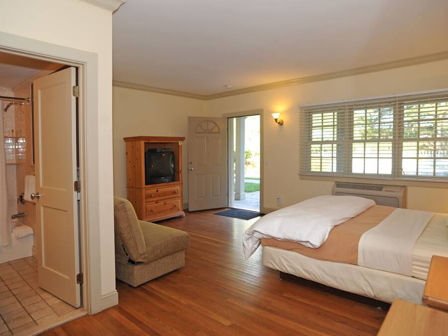 A bedroom with a bed, a wooden cabinet, a television, and a door leading to a bathroom.