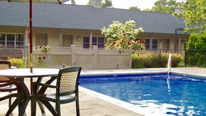 A swimming pool with a white fence, a table with chairs, and a building with a white picket fence in the background. - Southampton Long Island Hotel (Southampton)