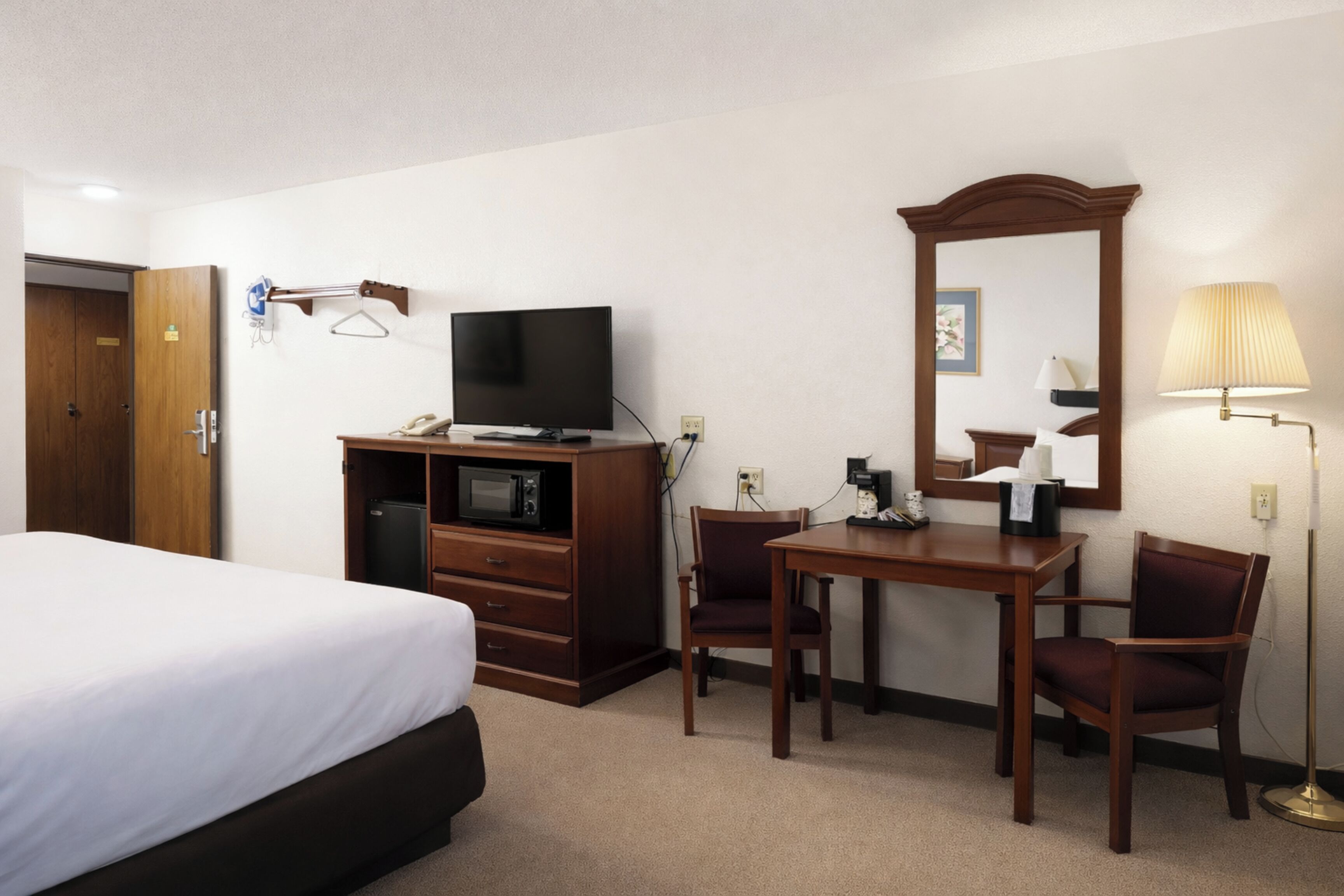 A hotel room with a bed, a TV, a desk with a chair, a mirror, and a lamp.