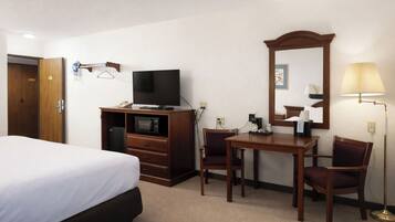 A hotel room with a bed, a TV, a desk with a chair, a mirror, and a lamp.