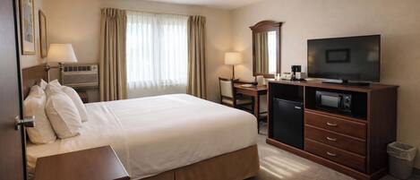A hotel room with a bed, desk, television, and a trash bin.