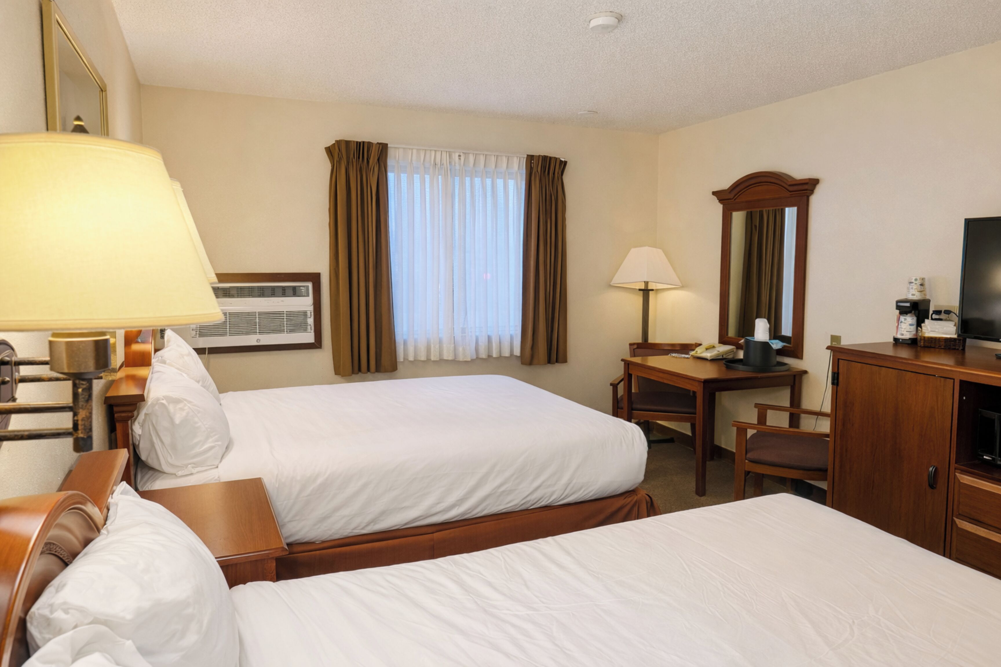 A hotel room with two beds, a desk with a chair, a television, and a mirror.