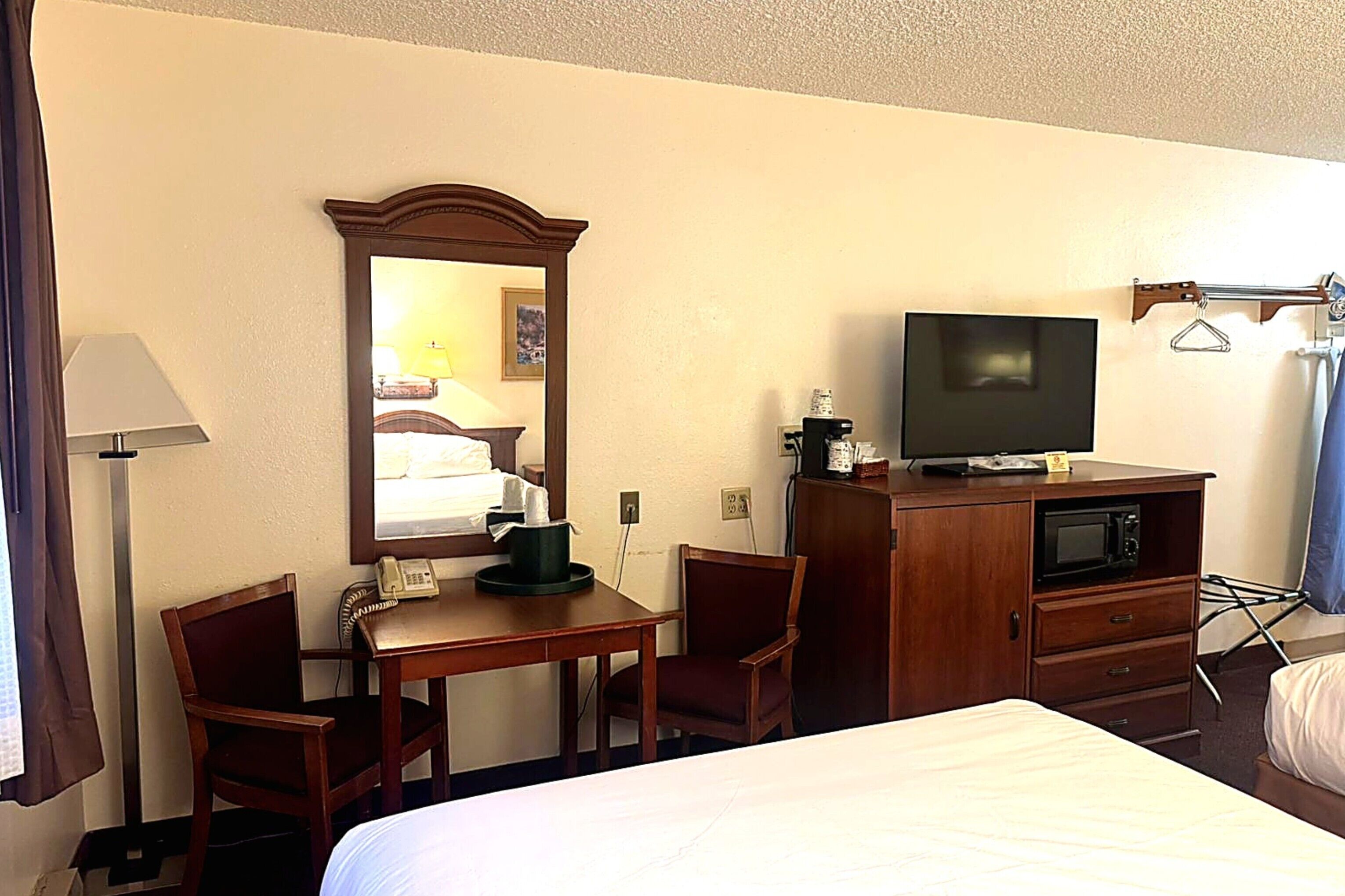A hotel room with a bed, a desk with a telephone, a television on a cabinet, and a mirror on the wall.