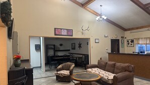 A spacious living area with a sofa, armchair, and coffee table, a dining area with chairs and a table, and a kitchen visible through an open doorway.