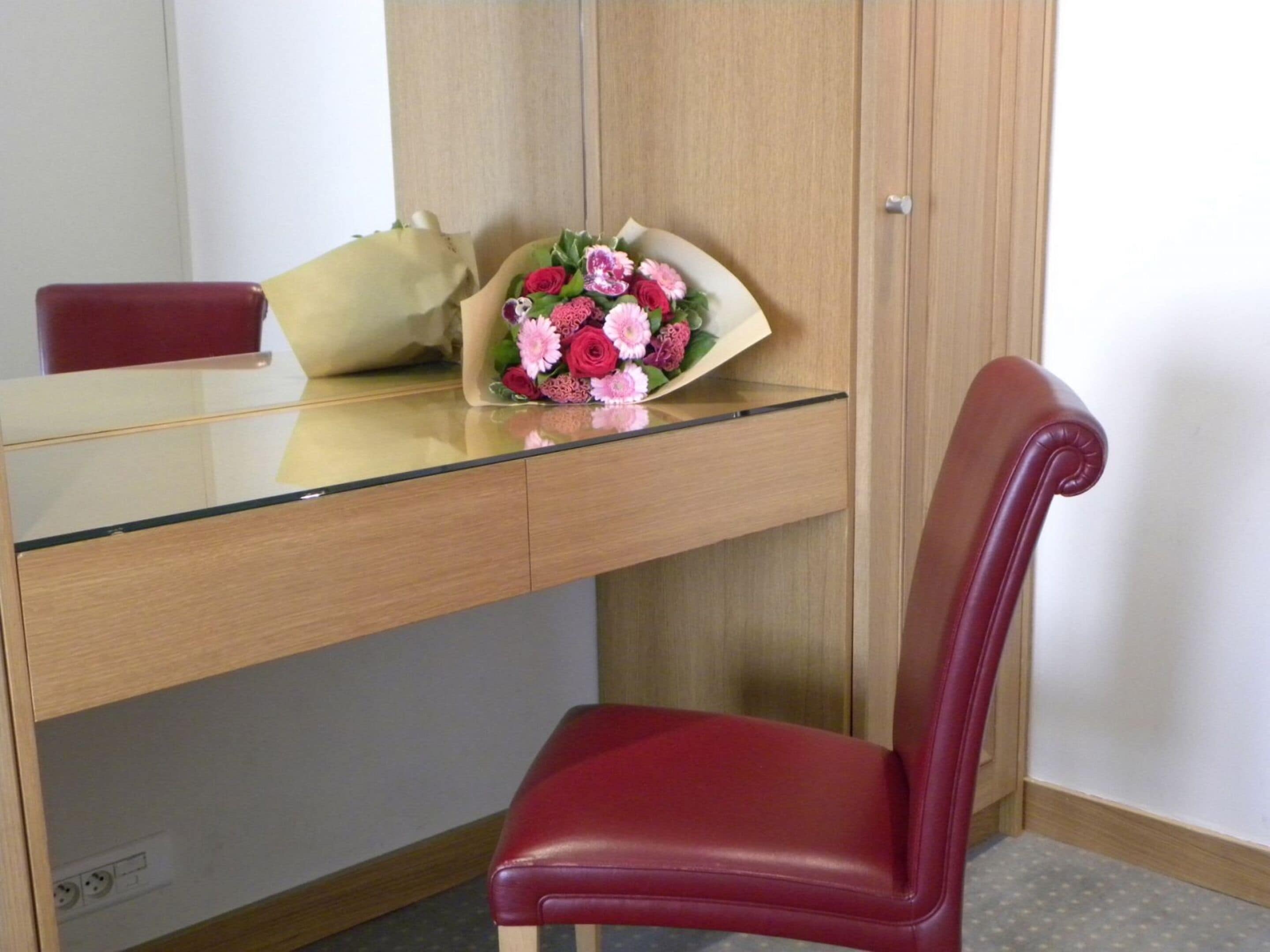 Ein Holztisch mit Glasplatte, ein roter Stuhl und ein Blumenstrauß auf dem Tisch.