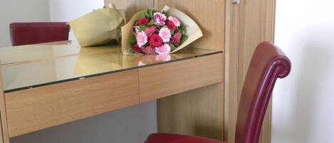 Un escritorio de madera con cubierta de vidrio, una silla roja y un ramo de flores sobre el escritorio.