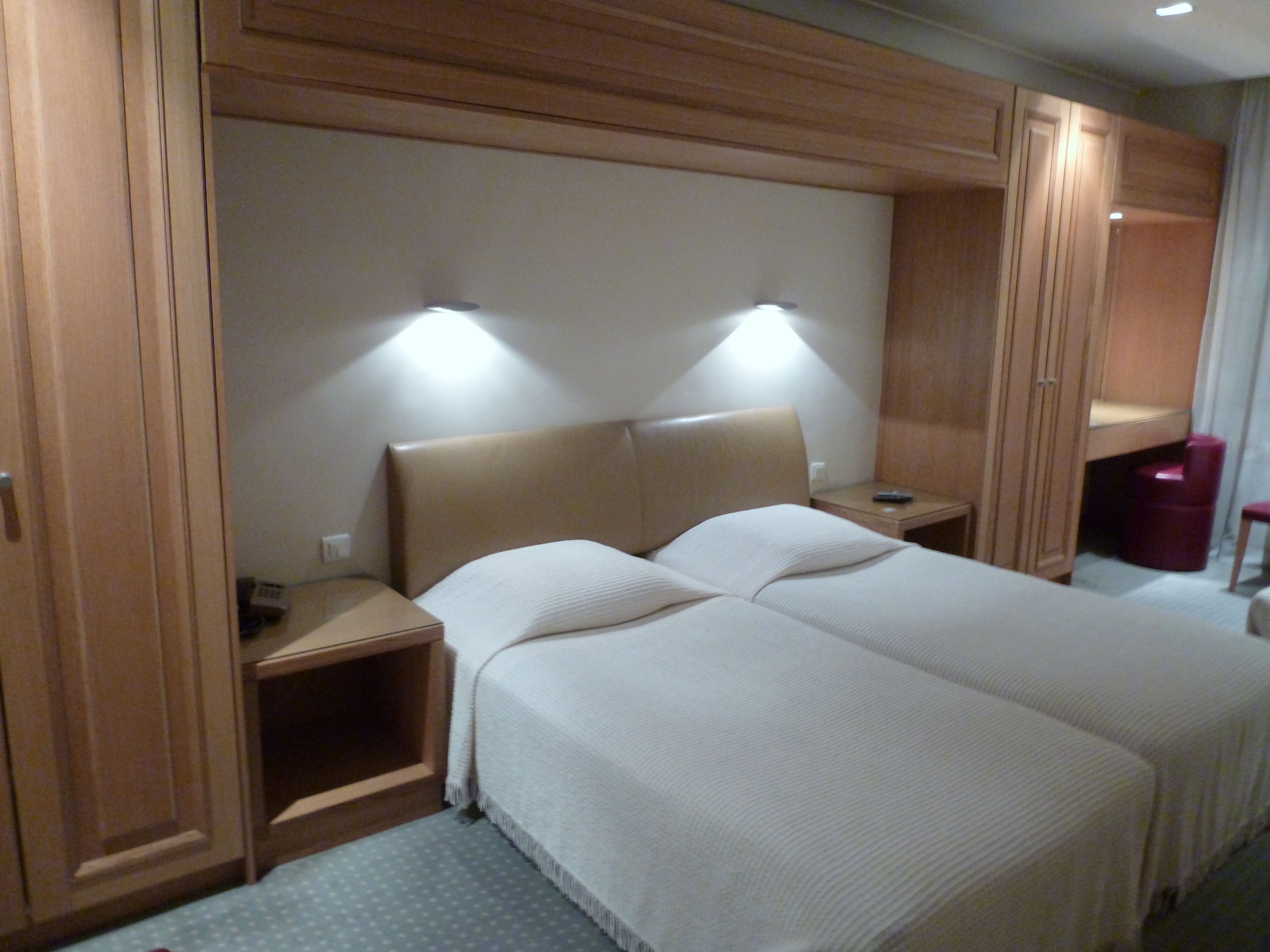 Ein Hotelzimmer mit Doppelbett, zwei Nachttischen, einem Kleiderschrank und einer kleinen Sitzecke.