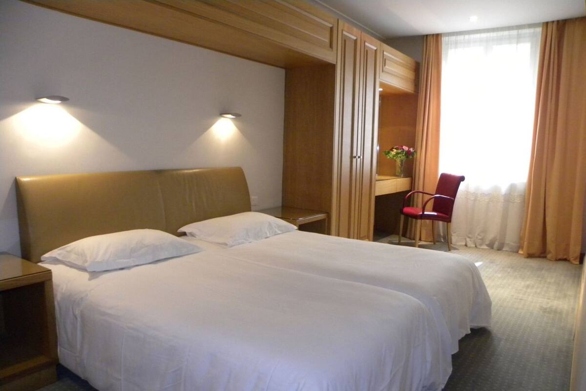 A hotel room with two beds, a desk, a chair, and a window with curtains.