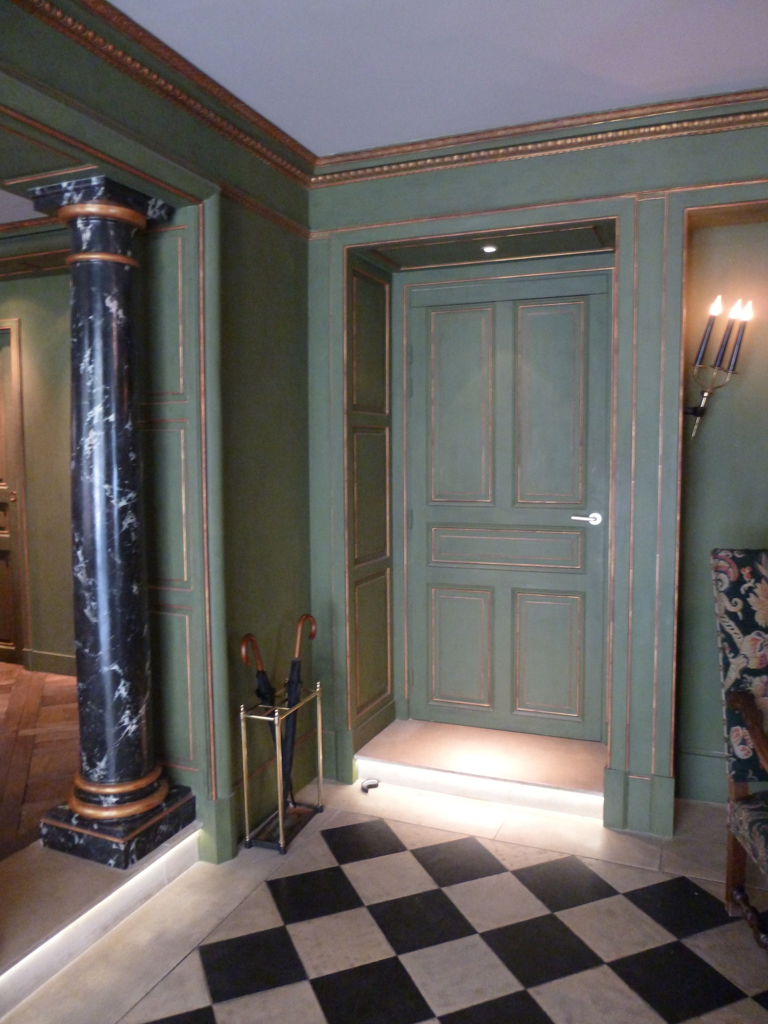 A room with a checkered floor, a door with a light underneath, and a pillar with a metal base.