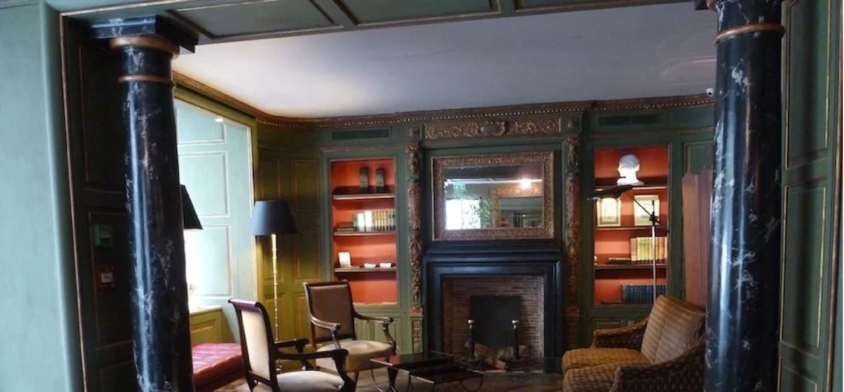 A room with a fireplace, bookshelves, a chair, and a lamp.