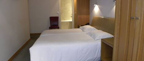 A hotel room with a large bed, a wooden wardrobe, a small chair, and a television mounted on the wall.