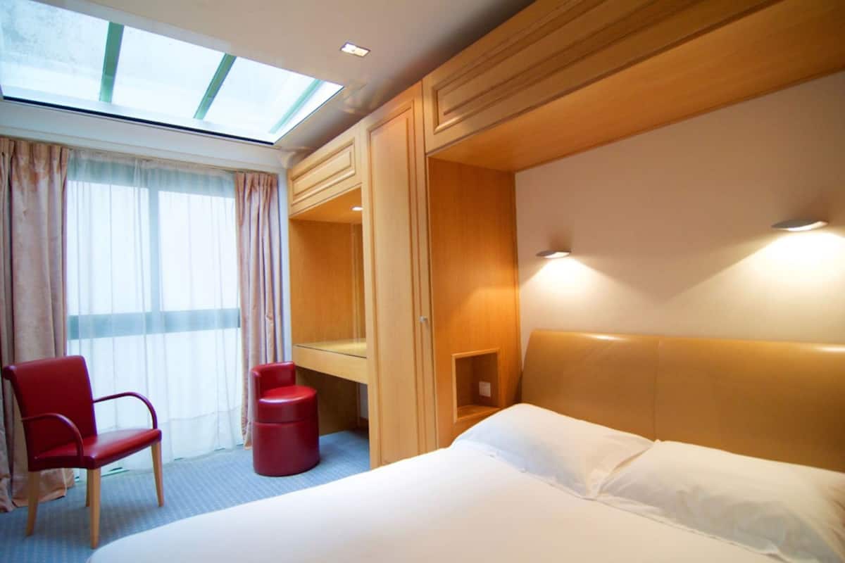 A hotel room with a bed, a desk, a chair, and a skylight.