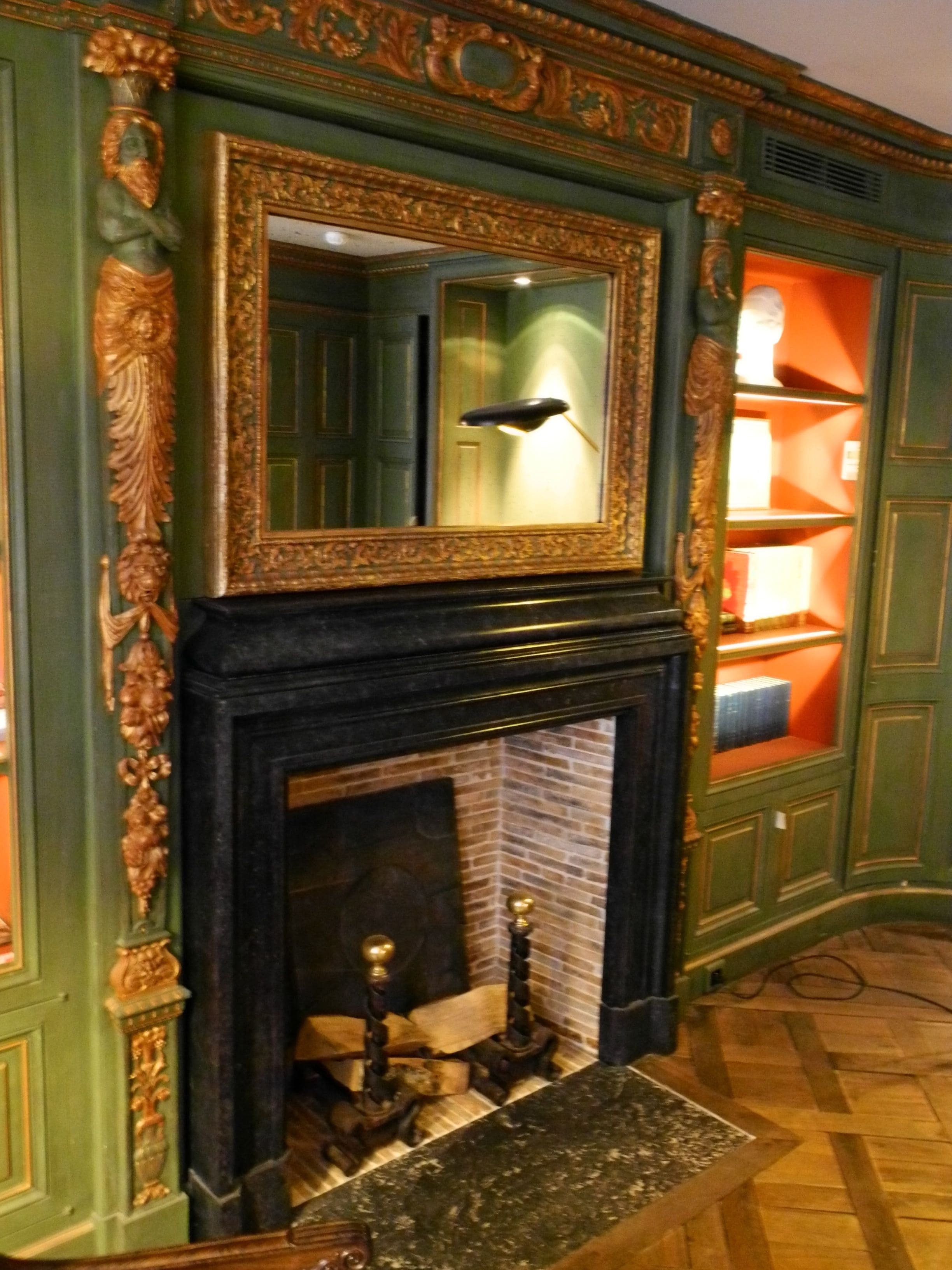 A room with a fireplace, ornate green walls, and a mirror above it.
