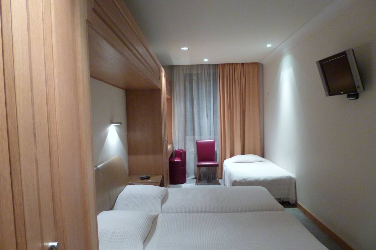 A hotel room with two beds, a TV, a chair, and a desk.