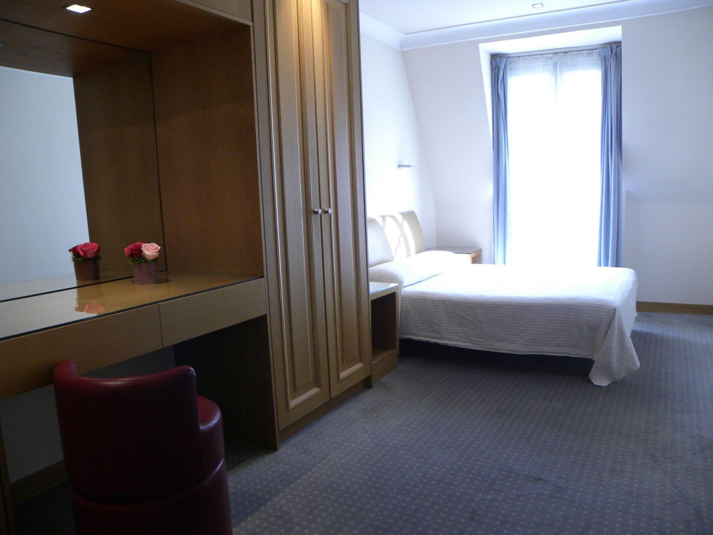 A hotel room with a bed, a desk, a chair, a wardrobe, and a window with curtains.
